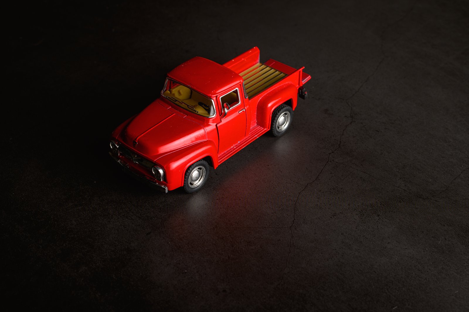 Red vintage pickup diecast model on a dark garage floor